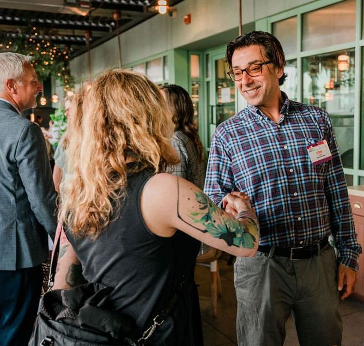 A man in glasses and a plaid shirt shakes hands with a woman with a floral tattoo on her arm during a Retreats Resources Lone Star State Roadshow.