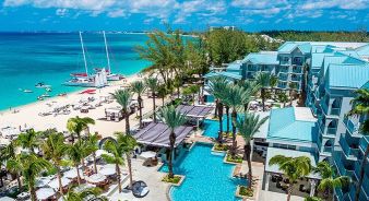 The Westin Grand Cayman Seven Mile Beach Resort & Spa - Cayman Islands, a beachfront resort features turquoise pools, palm trees, lounge areas, and direct access to a white sand beach with boats anchored nearby under a clear blue sky.