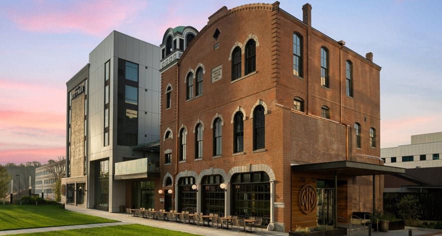 Hook & Ladder Sky Bar & Restaurant in a historic brick structure with arched windows; outdoor seating is visible along the sidewalk under a partly cloudy evening sky. There is a modern building is connected on the left side.
