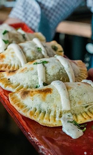 Close-up of three baked empanadas on a red plate, topped with a drizzle of white sauce and garnished with chopped herbs.