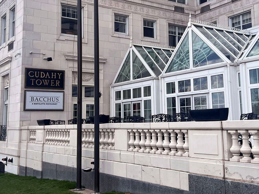 Exterior of Cudahy Tower featuring a glass-enclosed patio area and signage for Bacchus, a Bartolotta restaurant, on a cloudy day.