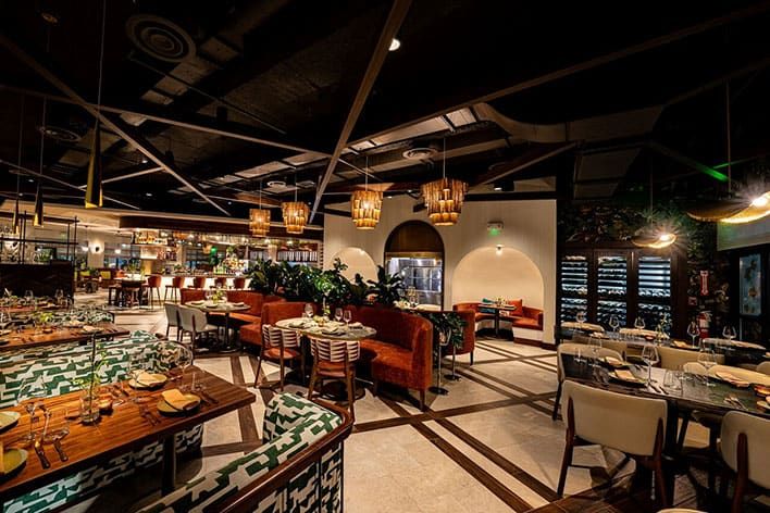 Chayote Barrio Kitchen - Modern restaurant interior with patterned booths, orange and white chairs, set tables, hanging lights, and a visible bar area in the background.