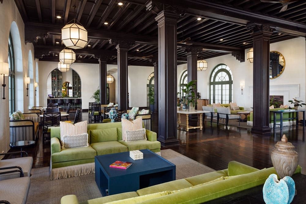 Spacious Casa Marina Key West lobby with green sofas, dark wooden beams, large arched windows, geometric pendant lights, and various seating areas.